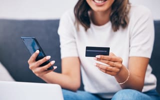 11 Finance Companies in Australia to Know A woman sits on a couch holding a smartphone in one hand and a credit card in the other.
