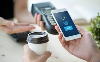 A close-up image of a hand holding a mobile phone with an illustration of an online payment platform on the screen.