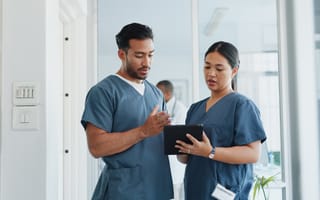 A pair of medical professionals wearing scrubs stand next to each other looking at a tablet screen.