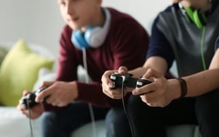 Two people sit side by side on a couch holding video game controllers.