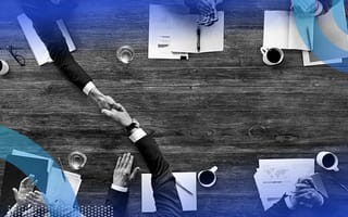An aerial shot of two groups of business people sitting across from each other shaking hands and clapping with papers and coffee on the table.