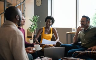 Group of young, smiling businesspeople talking together during a casual meeting in the lounge area of an office