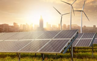 Solar panels and wind turbines in front of a city skyline.