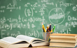 Photo of a classroom with a chalkboard in the background and textbooks on a desk.