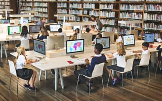 Several students sit at desks looking at desktop computer monitors.