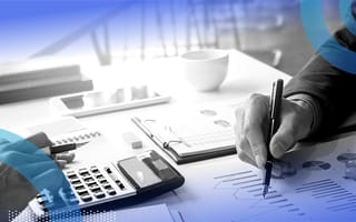 A closeup on two hands holding pens with a calculator doing math with spreadsheets nearby