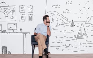 A man is seated in an office, with the walls behind him featuring drawings of a world map, charts and a seaside setting.