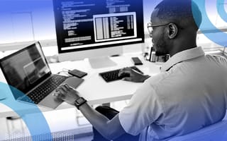 A computer engineer works on a laptop and a desktop terminal