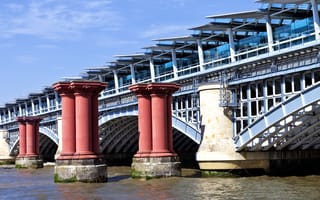 View from south bank of west side of arch wrought iron London Blackfriars Railway Bridge with platforms crossing River Thames in London along old red pillars, solar panels powered