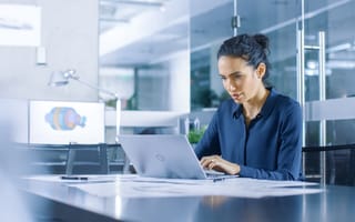 Woman sitting at a desk in a muted environment. She looks intently at the screen of a laptop and types.