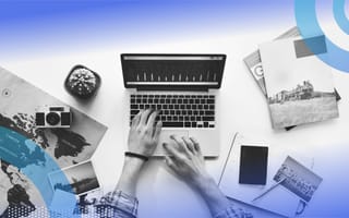 An aerial view of someone’s hands typing on a laptop surrounded by travel materials.