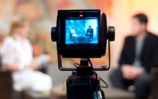 A camera films two media personalities in a TV studio.