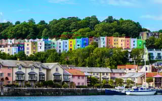 Landscape photo of Bristol featuring very colorful houses on the water, on a hill, as well s a boat on the water in the foreground..