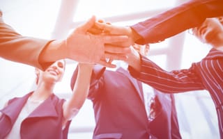 A team of professionals stacking their hands together in a gesture of unity.