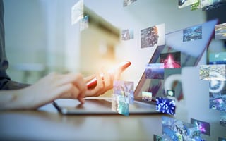 Person’s hands typing on a laptop screen while holding a phone, overlay of multiple screens seeming to move across the image, signifying multimedia images and videos.