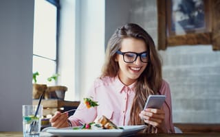 A woman eating a salad and looking at her phone is pictured.