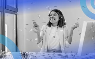 A business woman sitting at a computer desk, smiling with confetti raining down on her.