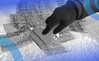 A close-up of a person’s hand scraping the ice off a car windshield.