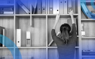 A woman reaching to grab a binder from a bookshelf/cubby hole that’s in disarray.