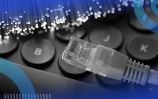 A close-up of the tip of an ethernet cord on top of a keyboard next to glowing optical fibers.