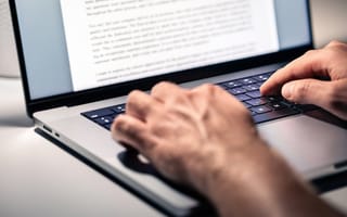 A close up of a pair of hands typing on a laptop keyboard.