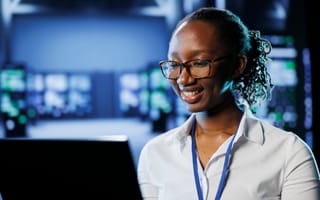 An IT professional smiles at a computer monitor.