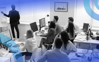 A presenter leads a workshop at a whiteboard in front of a room of people at computers