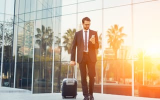A man in a suit holding a phone and a suitcase is shown.