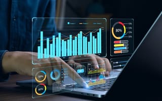 An illustration displaying a bar graph and other data visualizations hovers over a laptop keyboard as someone types.