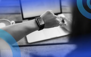 A person seated at a computer is checking their watch.