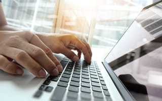 A close up of a pair of hands typing on a laptop keyboard.