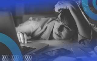 A young woman is slumped over her desk at work, staring wearily at her computer screen.