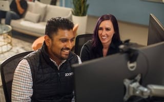 Two Zoom employees working next to one another, looking at screens and laughing.