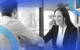 A young woman is smiling and shaking hands with a colleague.
