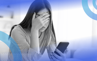 A woman holding a smartphone is covering her eyes and looking frustrated.