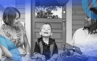 Two moms and their small son sitting on porch steps smiling, while one mom hands the boy a balloon.
