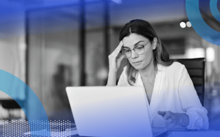 A woman wearing glasses and a weary expression is looking at a computer screen.