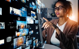 Woman pointing at her monitor, behind which a graphic display of multiple screens and data points is potrtuding, representing digital media and streaming