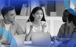 Four young professionals sitting at a desk with laptops having a discussion.
