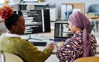 How These 12 Engineering Leaders Mastered the Art of Effective Communication Back view of two women software engineers discussing code on computer screen