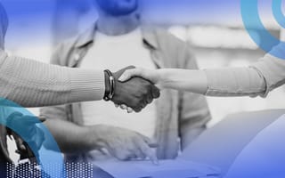 A white and a Black person shake hands over business documents held by a third person