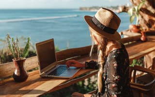 Woman coding on laptop on rooftop terrace overlooking ocean