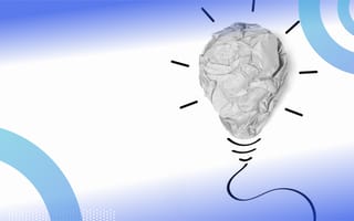 A crumpled up piece of paper in the shape of a lightbulb, with lines representing light drawn coming out of the lightbulb and lines underneath the lightbulb representing the base of it.