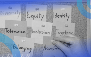 A close-up of a corkboard with sticky notes reading diversity, equity, identity, tolerance, inclusion, together, belonging and acceptance pinned to it. A person’s hand is actively pinning the acceptance note to the board.