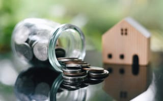 A spilled jar of coins sits in front of a wooden model of a house to symbolize home financing.