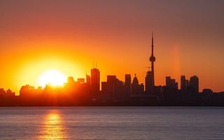 A view of the Toronto, Ontario skyline with the sun rising in the background.