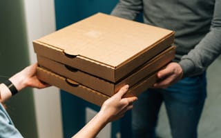 A close up of one pair of hands passing a stack of three pizza boxes to another pair of hands.