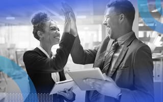 Two businesspeople high five while holding tablets