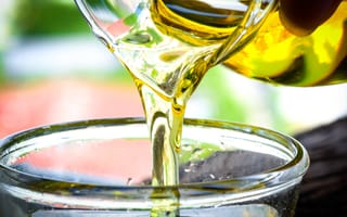 A close up of cooking oil being poured out of a glass pitcher and into another glass dish.