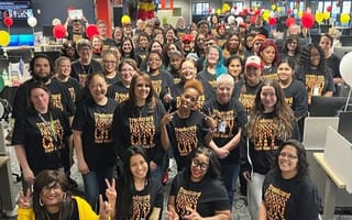 A large group of TrueML employees post in an office wearing matching shirts and surrounded by balloons.